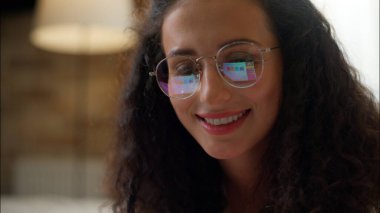 Gözlüklü, bilgisayar ekranına bakan gülümseyen bir kadın moda gözlüklü, beyaz bir kız yatakta dizüstü bilgisayarla alışveriş yaparken rahat bir hafta sonu geçiriyor yatak odasında dinleniyor.