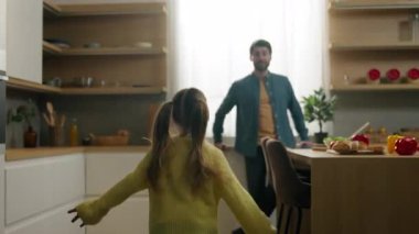 Mutfakta beyaz bir aile, mutlu bir ebeveyn, mutfakta mutlu bir baba, küçük bir çocuk, koşuyor, koşuyor, babasına koşuyor, faal bir baba, kalkıyor, dönüyor, evde dönüyor, sarılıyor, oyun oynuyor.