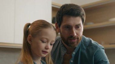 Kafkasyalı mutlu aile mutfakta bir bardak meyve suyu ile kaynaşıyor tatlı kız çocuk babasıyla birlikte bilgisayar kullanıyor ebeveyn kontrolü e-öğrenimi evde baba olmak dizüstü bilgisayarda yardımcı oluyor.