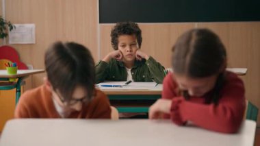 İki beyaz çocuk, erkek erkeğe gülüyor yalnız üzgün Afrikalı Amerikalı okul çocuğu hakkında konuşuyor. Tek başına ırkçı ayrımcılık yapıyor. Üç tane çok ırklı sınıf arkadaşı okul dersinde.