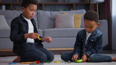 İki çocuk, oyuncaklı küçük Afrikalı Amerikalı çocuklar, etnik aile kardeşleri oynuyorlar. Kardeşler, rahat oturma odasında, yerde tamir oyunu oynuyorlar. Haftasonu evde vakit geçiriyorlar.