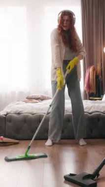 Beyaz kadın yerleri yıkamaktan mutlu. Kulaklıkla müzik dinliyor. Kulaklıkla şarkı söylüyor.