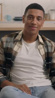 Evde gülümseyen, neşeli, samimi, genç, sakin, oturma odasında dinlenen Afro-Amerikan bir adam. Sadece haftasonu kanepede kameraya bakıyor.