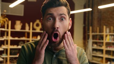 Hayretler içerisindeki beyaz erkek satıcı erkek çömlekçi erkek iş adamı küçük işletme sahibi kameraya bakıyor açık ağız şoku inanılmaz haberler içerideki çömlekçi dükkanında