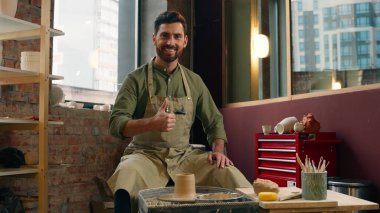 Mutlu yaratıcı, gülümseyen, beyaz, sanatçı, girişimci, küçük işletme sahibi, çömlekçi, kameraya bakan, el hareketi yapan, hobi olarak sanat atölyesindeki atölye çalışması gibi.