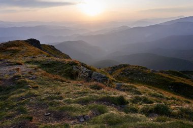 Dağlarda güzel bir yaz günbatımı. Yeşil çimenler ve taşlar. Dağ zirveleri saydam bulutlarla kaplıdır..