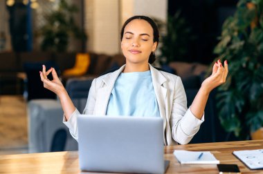 Meditasyon, rahatlama. Sakin, güzel, melez bir iş kadını, şirket çalışanı, risk müdürü, iş yerinde gözleri kapalı meditasyon yapan, işe ara veren, akıl sağlığını düşünen.