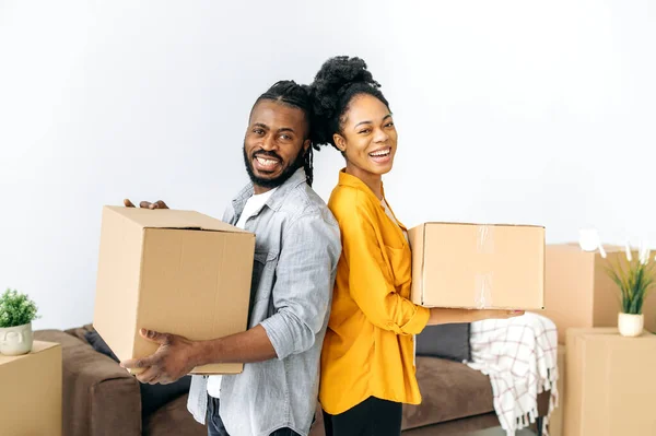 幸福的非洲裔美国夫妇 拿着装有房子用品的盒子 背对着彼此站着 看着相机 微笑着 为自己的公寓或房子感到高兴 — 图库照片