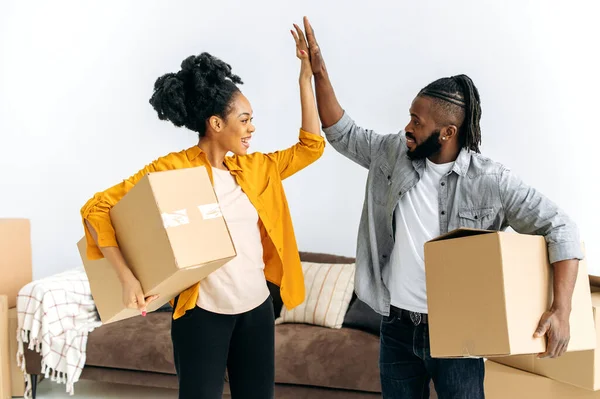 快乐快乐的非洲裔美国夫妇 拿着装有房子用品的盒子 站在客厅里 彼此互赠五块 为自己的房子或公寓感到高兴 — 图库照片