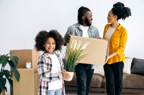 快乐的小非洲裔美国学龄前女孩拿着花盆 快乐的父母拿着纸盒 快乐的黑人家庭搬进新房子 买了他们的第一个家 迁移概念 — 图库照片