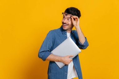 Gözlüklü, şık giyinmiş, elinde bir dizüstü bilgisayar tutan, boş alana şaşırmış, gözlük takan, gülümseyen, izole edilmiş turuncu arka planlı, fotokopi çeken,