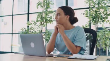 Dalgın odaklı bir ırk kadınının videosu, ofis çalışanı, yaratıcı yönetici, modern bir ofiste iş yerinde oturur, dizüstü bilgisayarına bakar, bir proje düşünür, strateji planlar.
