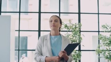 Modern trendy confident successful young brazilian or hispanic woman, wearing stylish business clothes, go across the creative office, holding documents in her hands, looking at the camera, smiling