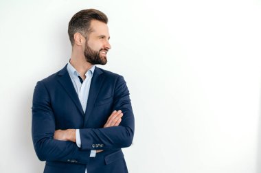 Positive attractive handsome caucasian successful bearded man in elegant suit, businessman, seo, standing over isolated white background with crossed arms, looking to the side, smiling friendly