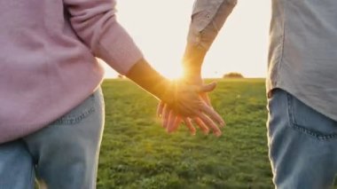 Close-up video of the hands of a man and a woman caucasian nationality tenderly holding each other while walking outdoors at sunset. Tenderness and romantic feelings