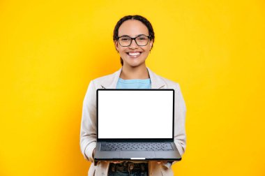 Pozitif, sevimli, gözlüklü, şık giyinmiş, elinde boş beyaz ekran dizüstü bilgisayarı olan, sunum için yeri olan, kameraya bakan, gülümseyen, izole edilmiş sarı arka plan.
