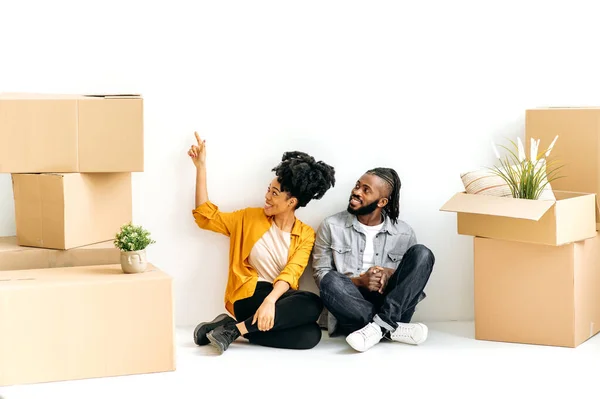 规划新公寓的未来室内设计 快乐的非洲裔美国夫妇坐在地板上 坐在装有家居用品的纸板箱中 计划修补他们的第一座房子 — 图库照片