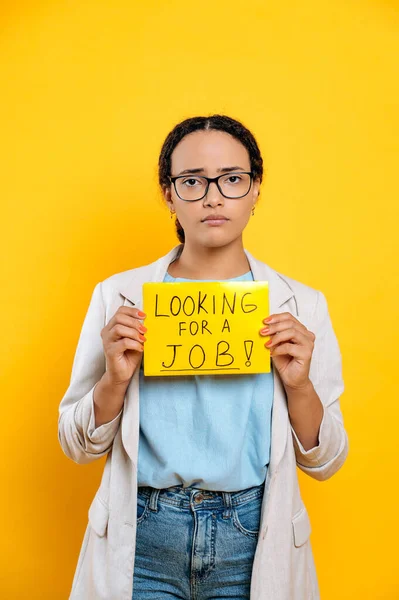 一个沮丧而又悲伤地混血的女人 一个寻找工作的有创意的专家 站在孤立的黄色背景上 带着寻找工作的标志 失望地看着镜头的纵向照片 — 图库照片