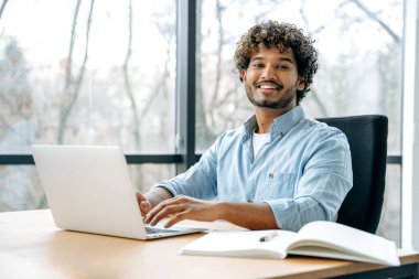 Gururlu Hintli adam, CEO, şirket çalışanı, yönetici, ofiste bir çalışma masasında oturuyor, yeni bir proje için dizüstü bilgisayarda çalışıyor, finansal iş planı, strateji, kamera görüntüsü, güler yüzlü arkadaş canlısı.