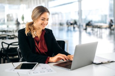 Başarılı bir Kafkasyalı iş kadını, yönetici, işe alım, ürün yöneticisi, iş merkezinde oturuyor, dizüstü bilgisayarda çalışıyor, bilgisayar ekranına bakıyor, gülümsüyor, sonuçtan memnun.