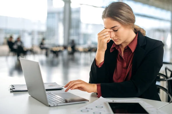Overworked exhausted frustrated caucasian woman, company employee, administrator or secretary, sits at her work desk, massages the bridge of her nose, feels tired from work, stress, headache