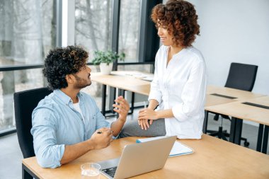 İşbirliği, ortaklık konsepti. Farklı etnik kökenden iki pozitif stil ortağı, bir erkek ve bir kadın, ofiste birlikte çalışıyorlar, beyin fırtınası yapıyorlar, fikirler ve stratejiler tartışıyorlar, gülümsüyorlar.