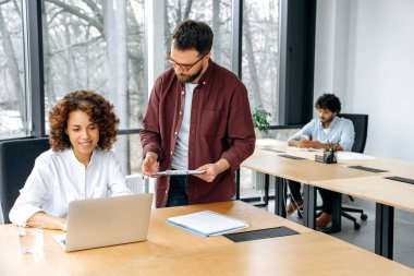 Farklı uluslardan başarılı iş arkadaşları, bir erkek ve bir kadın, modern ofiste birlikte çalışıyorlar, yeni proje için iş hedefleri ve fikirleri tartışıyorlar, planlama stratejisi ve promosyon, gülümseme