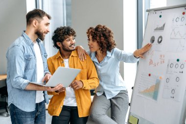 İşbirliği konsepti. Bir şirketin motive olmuş çok ırklı çalışanları, modern ofiste beyaz işaret panosunun yanında durmak, finansal istatistikleri analiz etmek, yönetim kurulundaki mali riskleri ve kârlılığı tahmin etmek.
