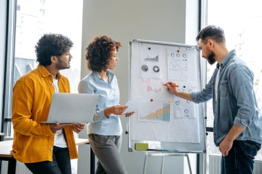 İşbirliği konsepti, takım çalışması. İş adamları yeni bir proje üzerinde birlikte çalışıyorlar, beyin fırtınası yapıyorlar, finansal grafiklerle beyaz tahtanın yanında duruyorlar, geliri tahmin ediyorlar, riskleri analiz ediyorlar, hedefler belirliyorlar.