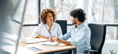 Farklı uluslardan iki çalışanın panoramik fotoğrafı modern bir ofiste yeni bir proje üzerinde birlikte çalışıyor, fikirleri ve hedefleri tartışıyor, iletişim kuruyor.