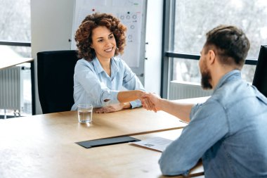 Ofiste bir masada oturan iki kişi, Afrikalı Amerikalı kadın ve beyaz adam başarılı bir iş görüşmesinden ya da iş görüşmesinden sonra el sıkışıyorlar, işbirliği üzerinde anlaştılar, sözleşme imzaladılar. Anlaştık, anlaştık.