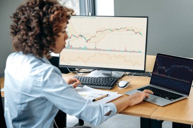 Başarılı bir Afro-Amerikan kadın tüccar, borsacı, borsacı, finans uzmanı, çalışma masasında oturuyor, bilgisayar ve çizelgeler kullanıyor, riskleri ve beklentileri analiz ediyor, kripto para biriminin yükselmesi veya düşmesi