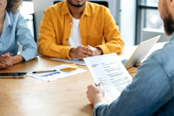 Interview with a job candidate. Close-up of a resume of a candidate in the hands of a hiring manager sitting in an office with a candidate for a new job, for a vacant position in a company