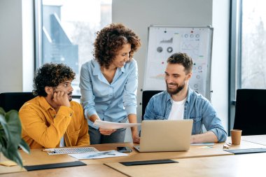 Bir grup pozitif çok ırklı yaratıcı motivasyona sahip tasarımcı, modern bir ofiste yeni bir tasarım projesi üzerinde çalışıyorlar, fikirleri tartışıyorlar, bir plan ve tasarım projesi hazırlıyorlar, gülümsüyorlar. Takım çalışması konsepti