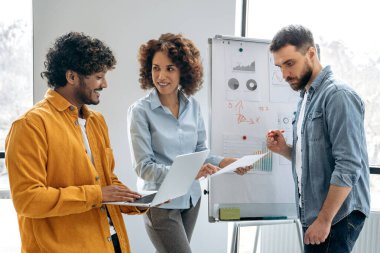 Takım çalışması konsepti. Olumlu, başarılı, çok ırklı meslektaşlar, ofis çalışanları, yöneticiler, işaretleme tahtasının yanındaki modern bir ofiste durun, mali tabloları analiz edin ve tartışın, kar, riskler