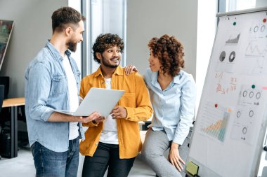 Farklı milletlerden başarılı meslektaşlar, ofis çalışanları, yöneticiler, işaretleme tahtasının yanındaki modern bir ofiste duruyorlar, mali tabloları analiz ediyorlar ve tartışıyorlar, kar, riskler,
