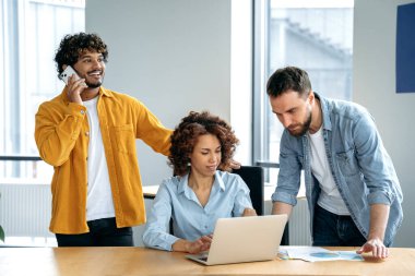 Takım çalışması konsepti. Başarılı çok ırklı iş adamlarından oluşan yaratıcı bir grup, ofiste bir proje üzerinde birlikte çalışıyorlar, dizüstü bilgisayar kullanıyorlar, fikirleri tartışıyorlar, beyin fırtınası yapıyorlar, birbirleriyle iletişim kuruyorlar, gülümsüyorlar.
