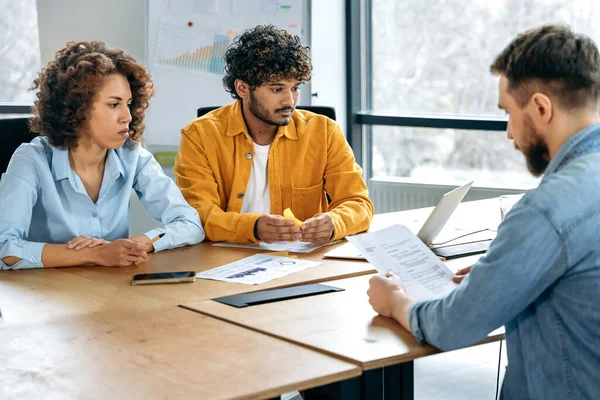 Interview with a job candidates. A resume of a candidate in the hands of a hiring manager sitting in an office with two candidates for a new job, for a vacant position in a company