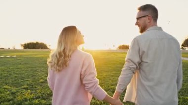 Gün batımında yürüyen harika bir çift. Mutlu Kafkas tarzı aşık eşler, gün batımında dışarıda yürüyorlar, nazikçe sarılıyorlar, öpüşüyorlar, vakit geçiriyorlar, el ele tutuşuyorlar, birbirlerine sevgiyle bakıyorlar, gülümsüyorlar.