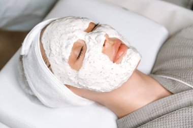 Cilt bakımı, güzellik prosedürleri, spa günü. Güzeller güzeli bir kadının yakından çekilmiş yüzü. Gözleri kapalı bir şekilde salonda yatıyor. Yüzünde nemlendirici anti-yaşlanma maskesi var.