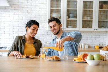 Mutlu çok ırklı çift, beyaz erkek ve Afrikalı Amerikalı kadın, hafta sonu kahvaltısında birlikte vakit geçiriyorlar, kahve içiyorlar, kruvasan yiyorlar, farklı konular hakkında sohbet ediyorlar, boş zamanları planlıyorlar, gülümsüyorlar.