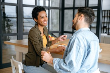 Birlikte vakit geçirmek. Mutlu aile çifti, beyaz erkek ve Afrikalı Amerikalı kadın, mutfakta sağlıklı yulaf lapasıyla kahvaltı yapıyorlar, hafta sonları birlikte vakit geçiriyorlar, iletişim kuruyorlar, gülümsüyorlar.