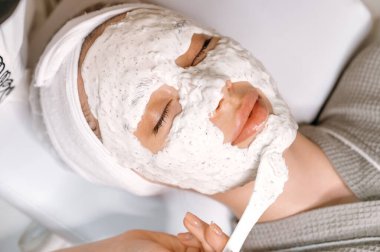 Güzellik uzmanı yüzüne nemlendirici maske takarken, güzel bir kadının kuaförde gözleri kapalı yatışı. Nemlendirici yüz maskesi, fırça, besleyici deri. Güzellik prosedürü