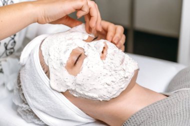 Kadının yüzündeki maskeyi çıkarmanın yakın plan görüntüsü. Kadın yüzünde nemlendirici yüz maskesi, ovalama, besleyici deri. Deri bakımı konsepti. Güzellik prosedürü