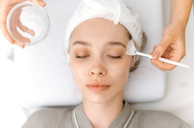 Güzellik prosedürü. Kozmetik uzmanı maske takmadan önce güzel beyaz bir kadının yüzünü özel jöle ile temizler. Üst Manzara. Güzellik salonunda yüz bakımı prosedürleri