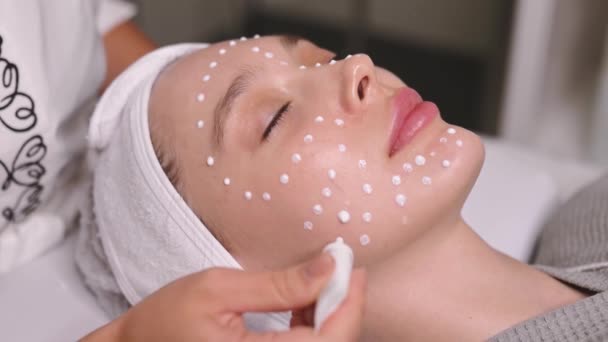 美容学概念 美容院的护理程序一个年轻漂亮的女人脸上的润肤霜 美容师将抗衰老霜应用于病人的面部 以防止皱纹过早 — 图库视频影像