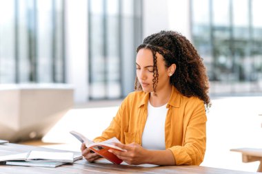 Kendine güvenen, Brezilyalı ya da İspanyol kıvırcık saçlı genç bir kadın, elinde kitapla dışarıda oturuyor, ilginç kitaplar okuyor, bilgi topluyor, ilham alıyor. Okuma konsepti