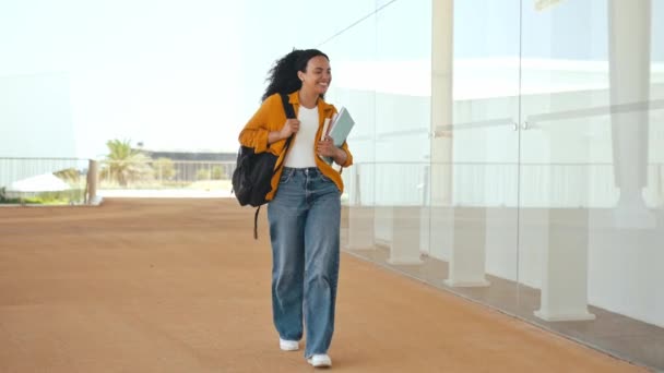 バックパック ノートを手に 彼女の手の中に 大学の近くを歩いて 離れて見て 完成した学校の日と陽気な驚くべき巻き毛混合レースの女性学生のフル長さの写真 — ストック動画