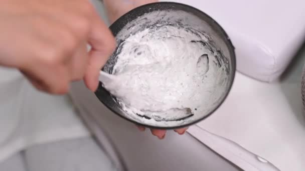스크럽 화장품 전문가는 마스크 찰흙을 그릇에 얼굴에 섞는다 미용실에서 화장품 스톡 비디오