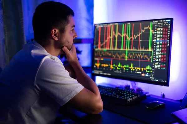 Stock market, online trading, analysing datum and risks, cryptocurrency concept. Successful male trader in sitting in a dark room checking cryptocurrency information data on finance market graph